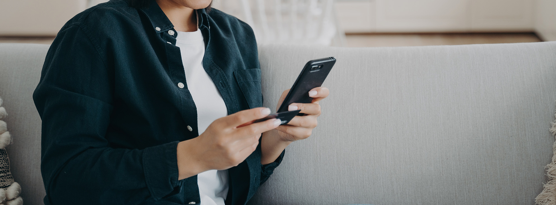 Woman holding bank credit card smartphone makes successful cashless payment sitting on sofa at home