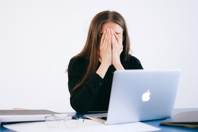 woman covering face sitting at computer