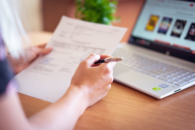 person holding paper and pen near computer